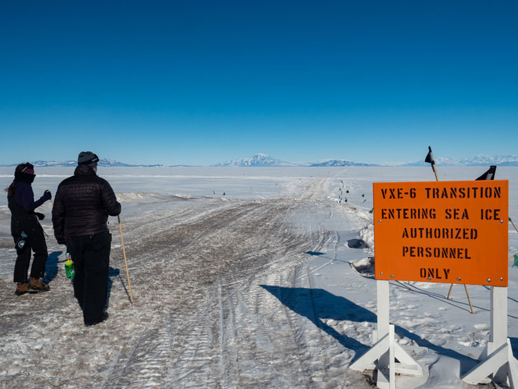 Two people at beginning of sea ice trail signed with authorized personnel only.