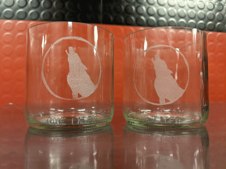 Two glasses crafted from bottle bottoms and etched with design of howling wolf.