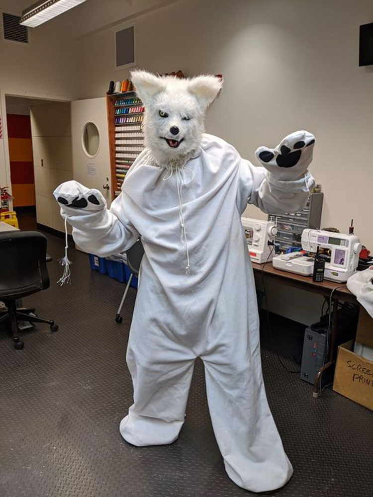 Person standing with “paws up” in white wolf costume.