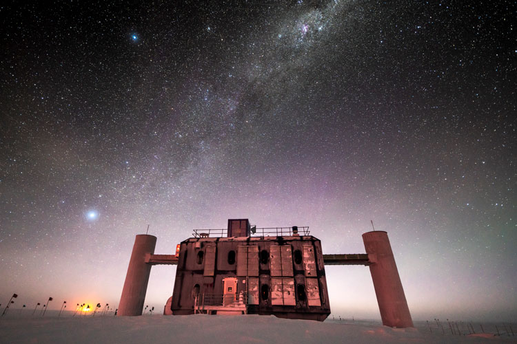 Front view of the IceCube Lab at twilight, stars in sky and sunlight just barely on horizon.