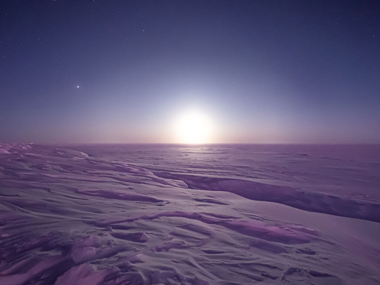 Icy barren landscape at South Pole with bright moon on horizon