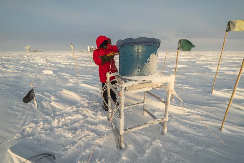Person in red parka placing a cover on a field site IceAct telescope at the South Pole.