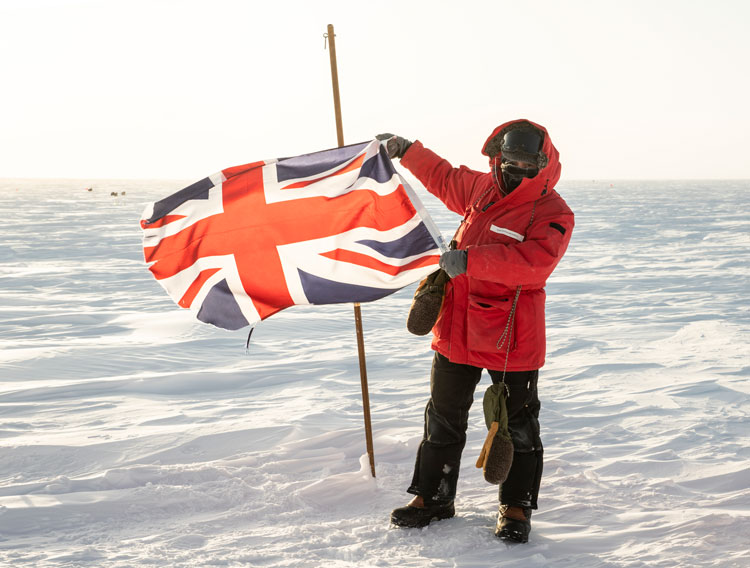 IceCube winterover Josh standing next to British flag.