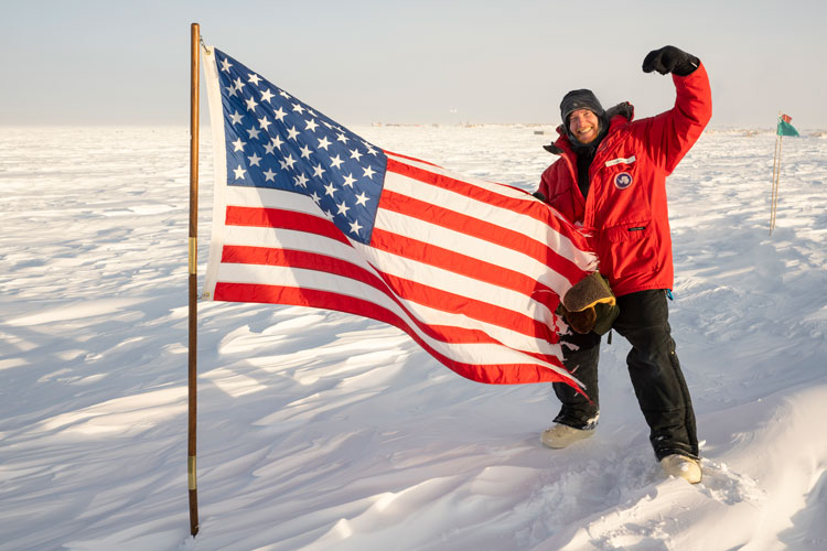 IceCube winterover Martin standing next to US flag.