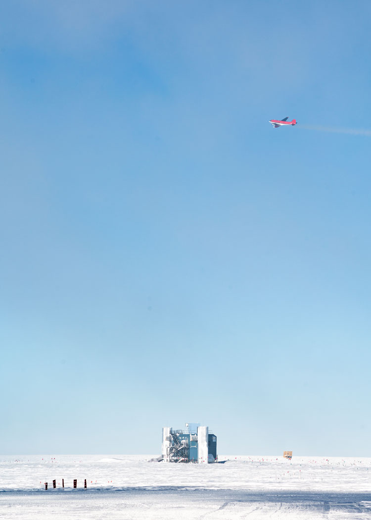 A red airplane high above the IceCube Lab, with clear blue skies.