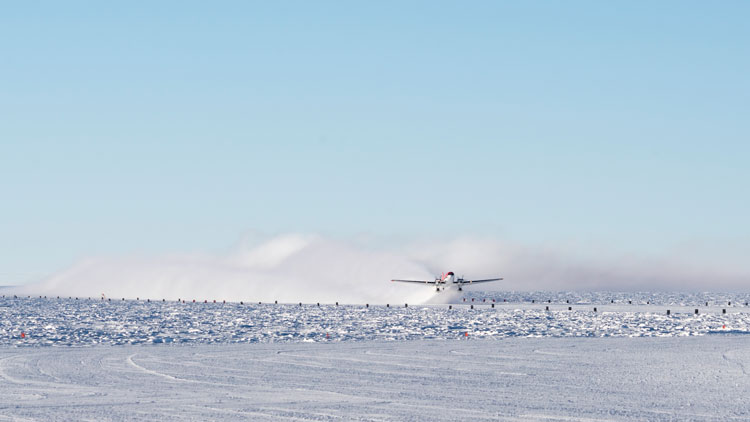 Airplane in distance, taking off from South Pole icy surface.