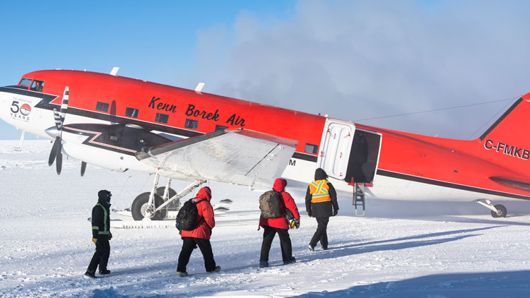 Two winterovers in red parkas approaching an airplane on the ground for departure.
