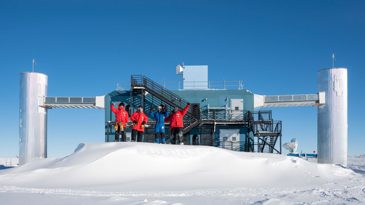 Four winterovers posing on snowdrift in front of the IceCube Lab.