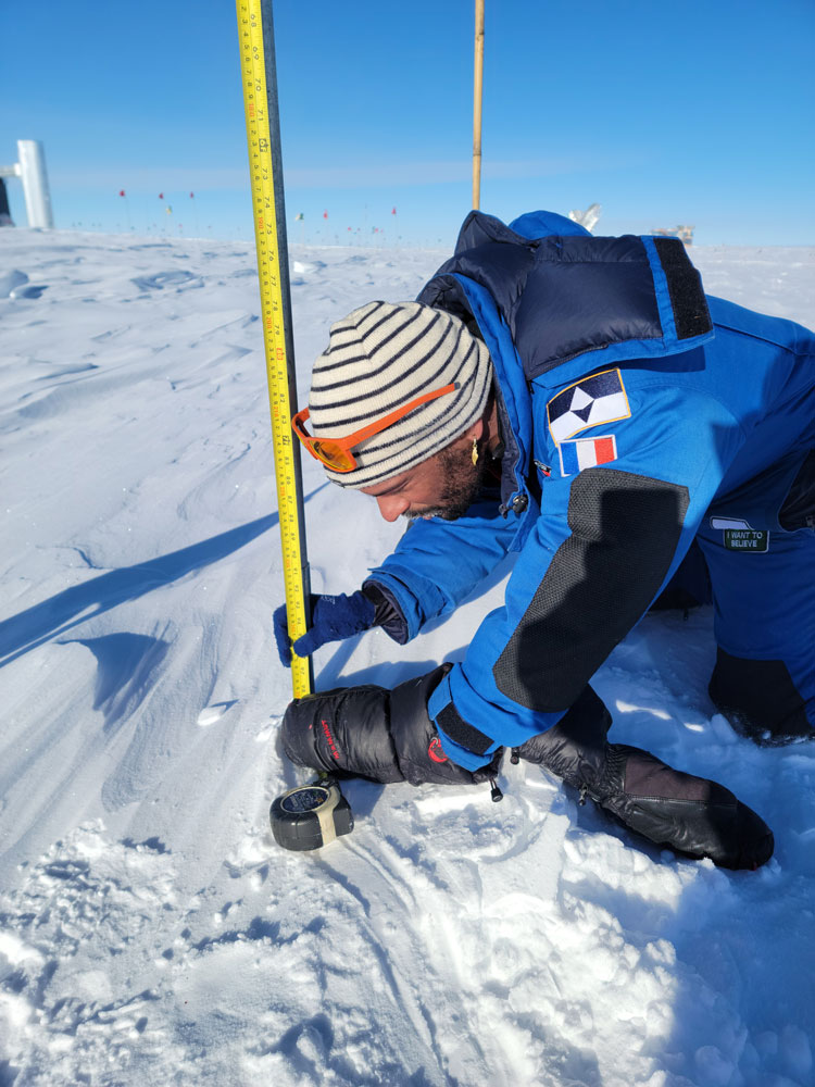Close-up of person in blue parka crouched down to take a snow measurement.