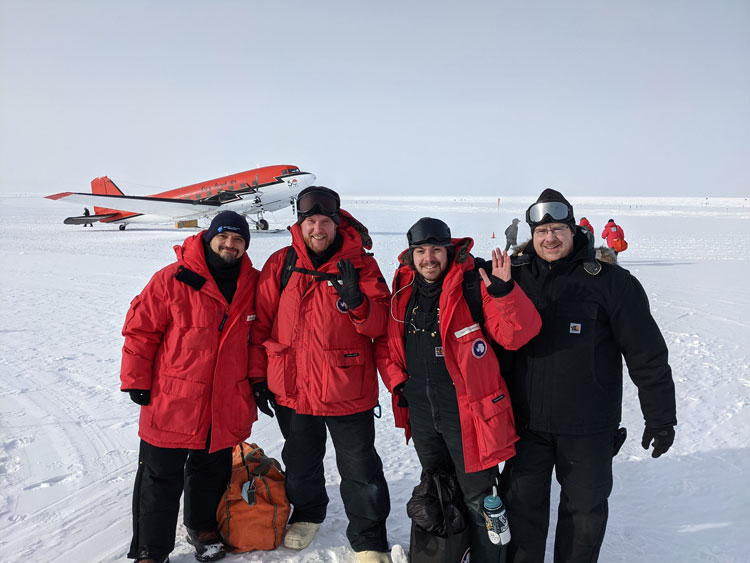 Four winterovers in parkas posing with a small airplane on the ice behind them.