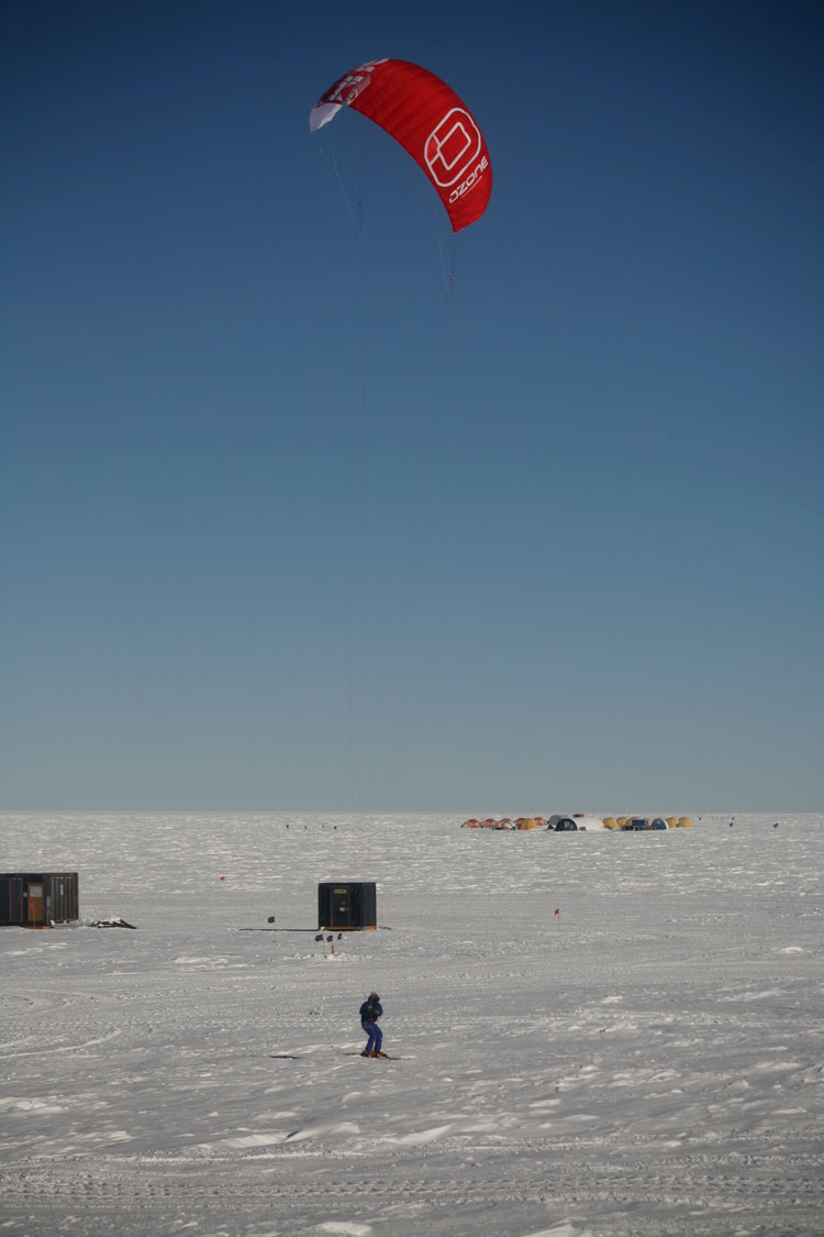 Person out trying to kite-ski at the South Pole, with kite high above then in clear sky.