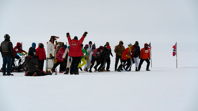Group of a dozen or so people walking or running in a race on the ice at the South Pole.