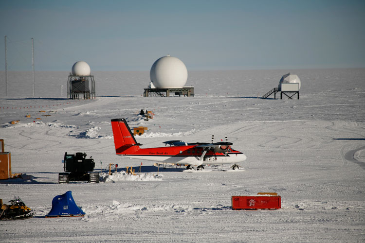Small plane parked at the South Pole with three satellite domes in background.