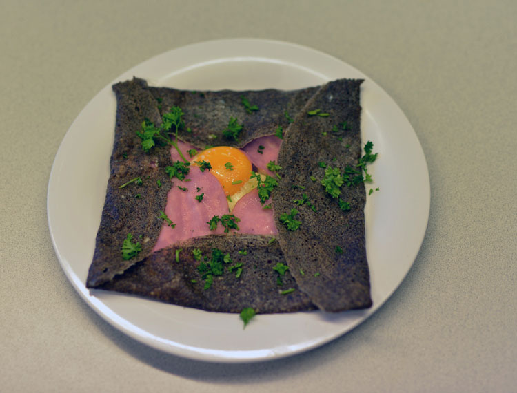 Close-up of a plated savory buckwheat crepe, squared off with edges folded partway up.