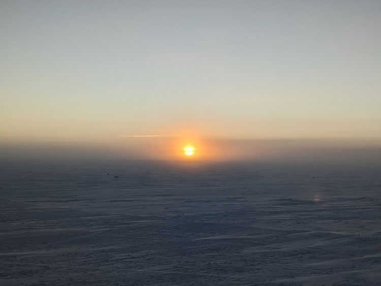 Orange sun low on horizon at the South Pole.