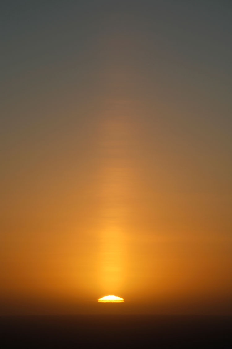 Vertical image showing a sun pillar extending straight up from the setting sun.