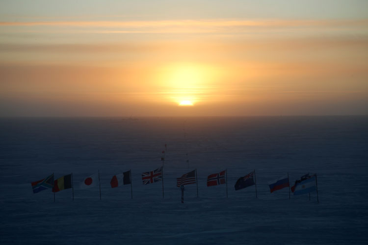Sun setting over the line-up of flags at the ceremonial South Pole.