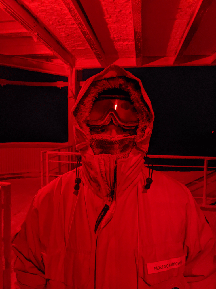 Close-up under red light of a winterover outside in full cold weather gear.