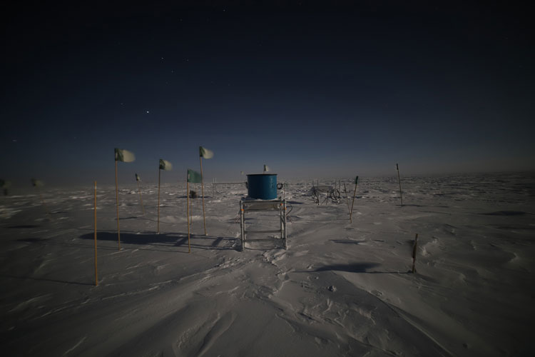 A telescope (blue tub-like structure on a stand), out in the snow-swept Antarctic plain.
