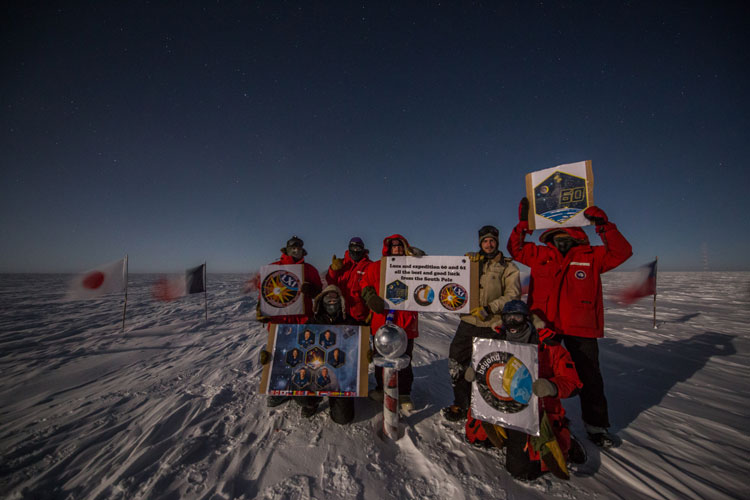 group photo holding signs up, outdoors at the South Pole