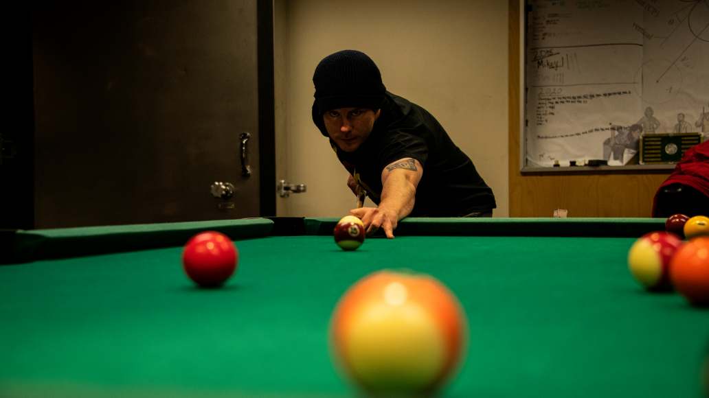 Facing person about to hit a pool ball with pool stick