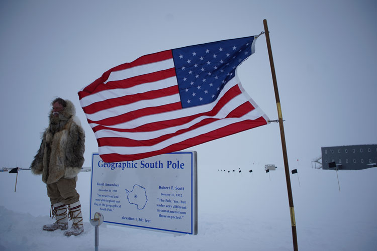 Someone dressed up like Roald Amundsen posing at the geographic South Pole sign