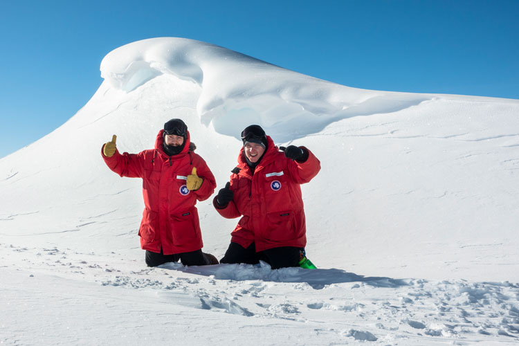 Two winterovers giving thumbs up in front of large snowdrift