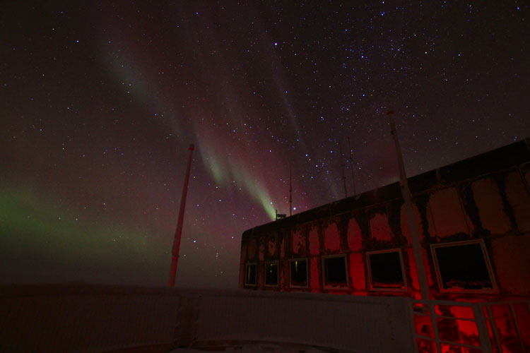 wispy lines of aurora against starry sky, station in foreground