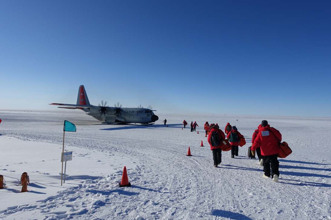 Group of people in red parkas walking toward a plane at the South Pole