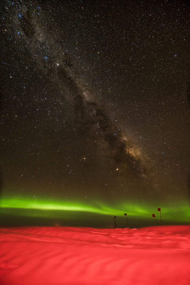 Milky Way over green horizontal band of auroras over flagline bathed in red light