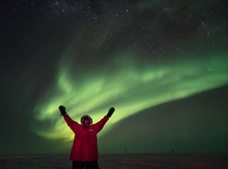 Arms up in air with bright aurora in sky