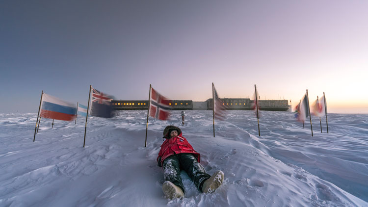 Person lying on snow at ceremonial South Pole