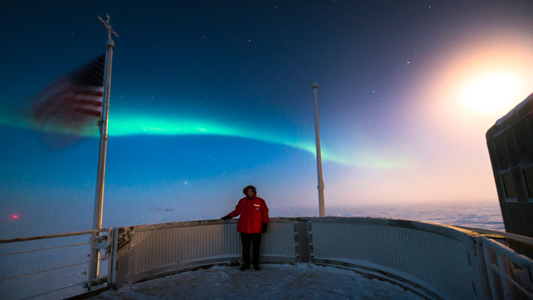 Martin on observation deck at South Pole station, with bright moon and auroras