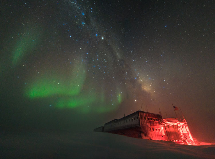 South Pole station lit in red with stars and auroras overhead