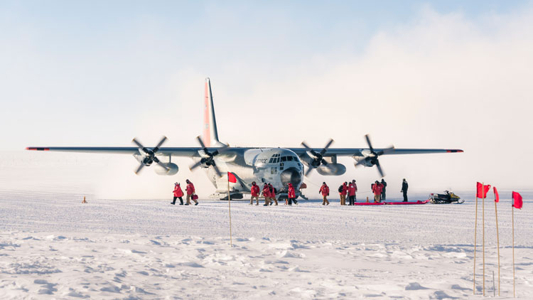Group of people in red parkas debarking plane on skiway at South Pole
