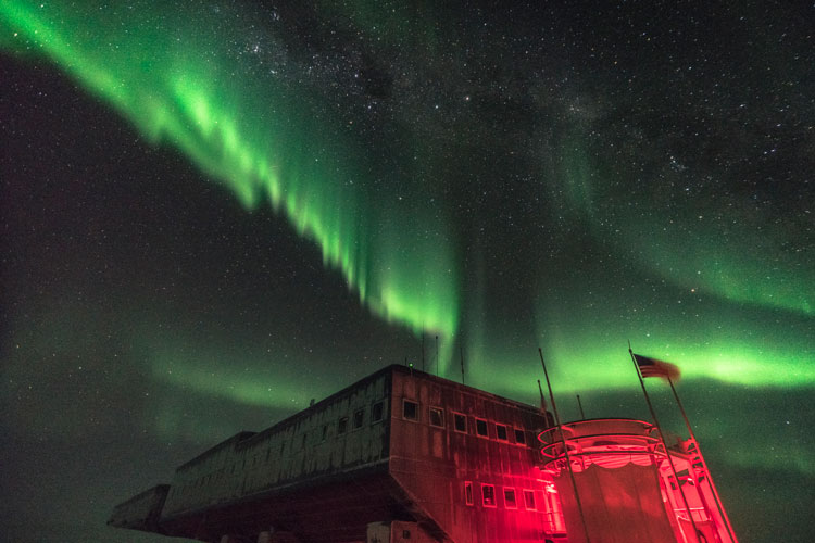 Bright green streak of aurora over South Pole station bathed in red light