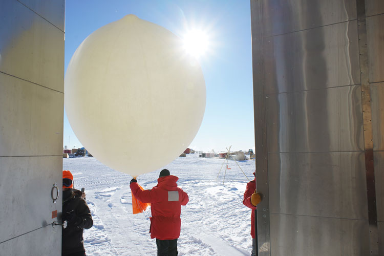 Person in red parka from behind, holding onto large weather balloon framed in doorway