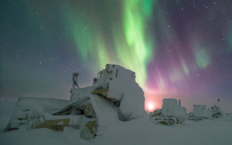 Snowed-in bulldozer at South Pole with aurora in sky