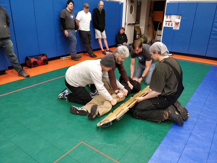 Group crouched around person to put on stretcher in fire rescue training