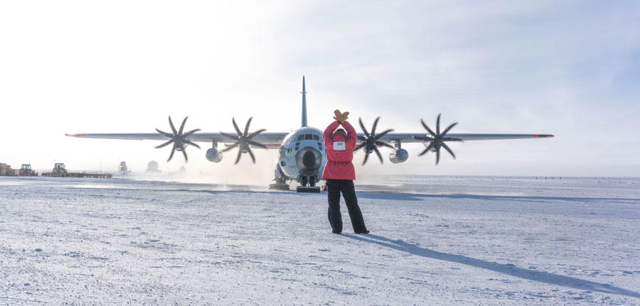 Person in red parka shown from behind, waving in a plane taxiing on the ice