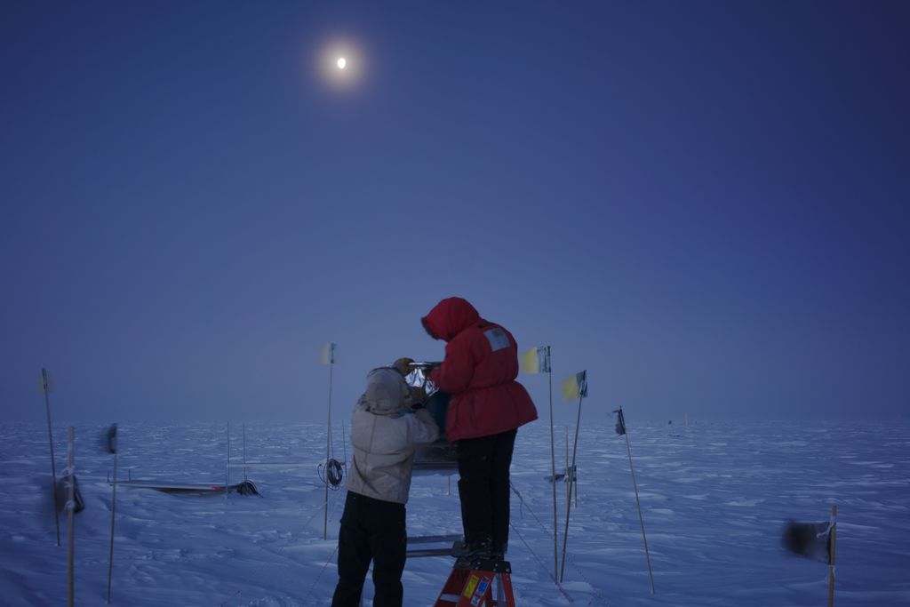 Two people covering up an instrument outside at the South Pole