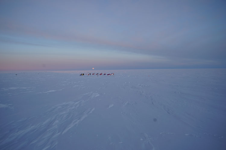 Icy blue landscape, with moonrise just at horizon, seen above ceremonial South Pole