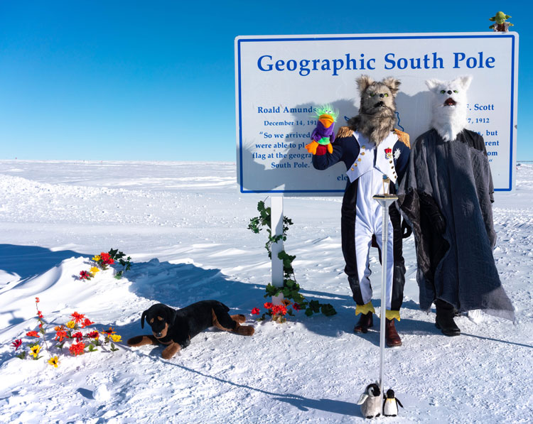 Two costumed people standing in front of geographic South Pole sign, with miscellaneous decorations scattered about