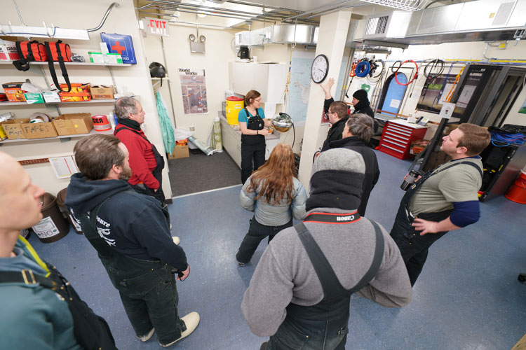 Group standing in semi-circle around presenter near an IceCube DOM