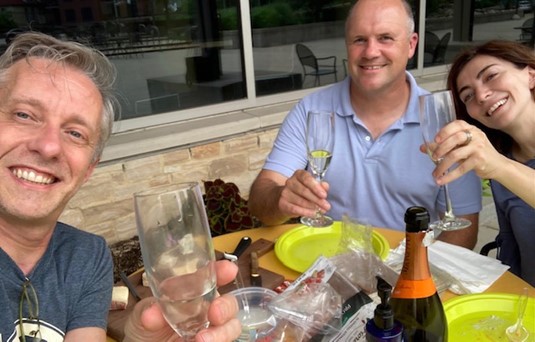 From L to R: Paolo Desiati, Kieran Furlong, and Elena D’Onghia sitting at a table on the Terrace toasting with champagne flutes.