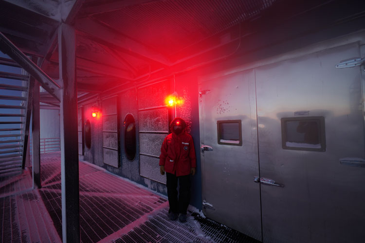 Person in red parka, with red headlamp, outside station with red lights on