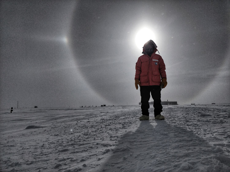 Person standing with their head almost centered on the sun, with halo and sun dogs surrounding