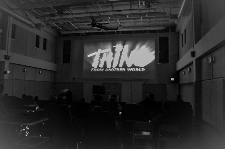 B&W image of station gym, The Thing on screen