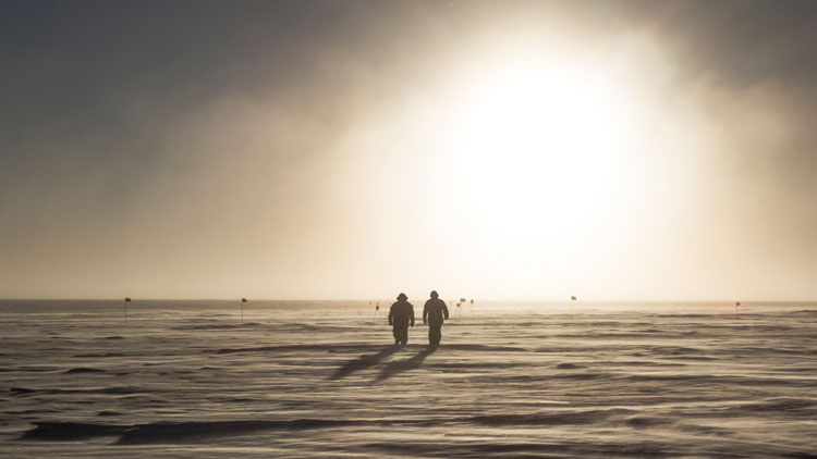 Two people walking on snow, from a distance.