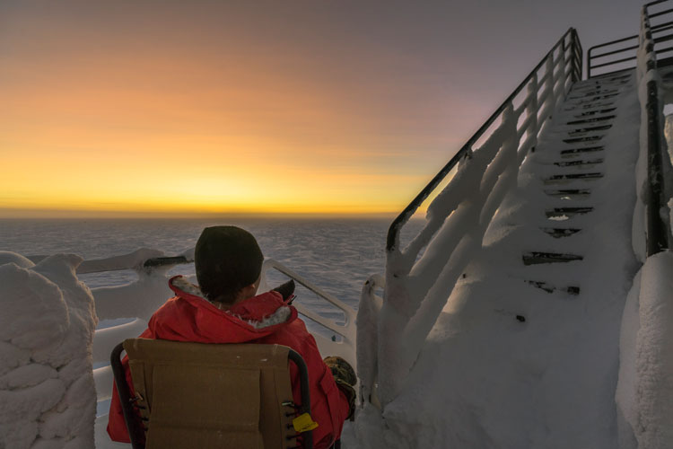 Seated person, back to camera, outside at South Pole as sun rises
